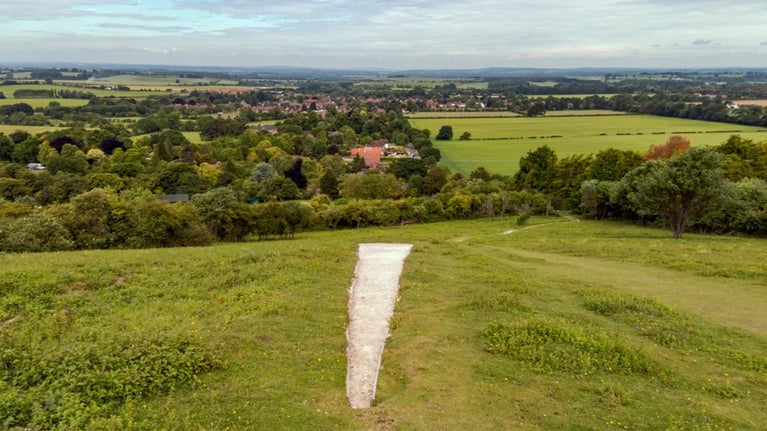 Large white chalk mark on hill overlooking green valley with settlement in the distance